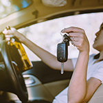 person sitting in the driver’s seat of a car, holding a car key in one hand and an open bottle